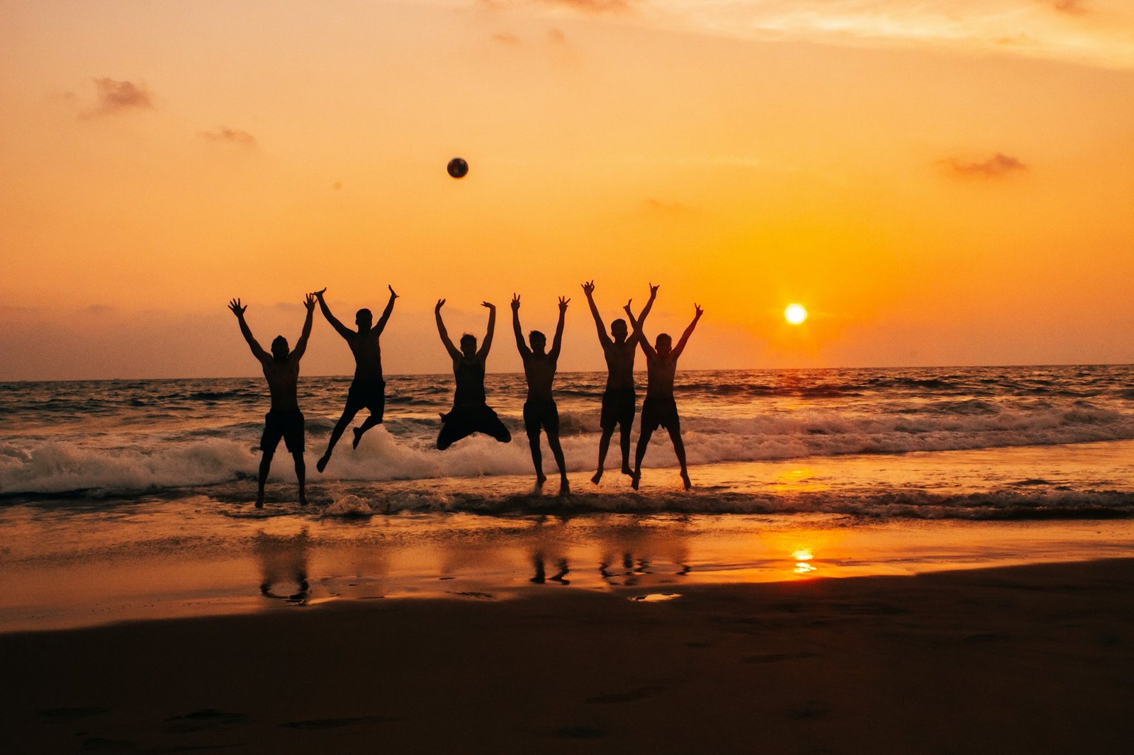 Friends jumping for joy on the shore at sunset